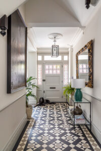 A modern entryway featuring decorative tile flooring, a small dog resting, and stylish decor including a green lamp and a mirror.